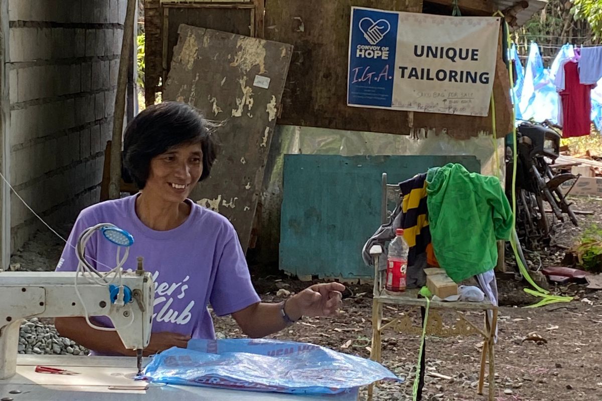 Nanay Unie sews in front of a sign that says "Unique Tailoring."