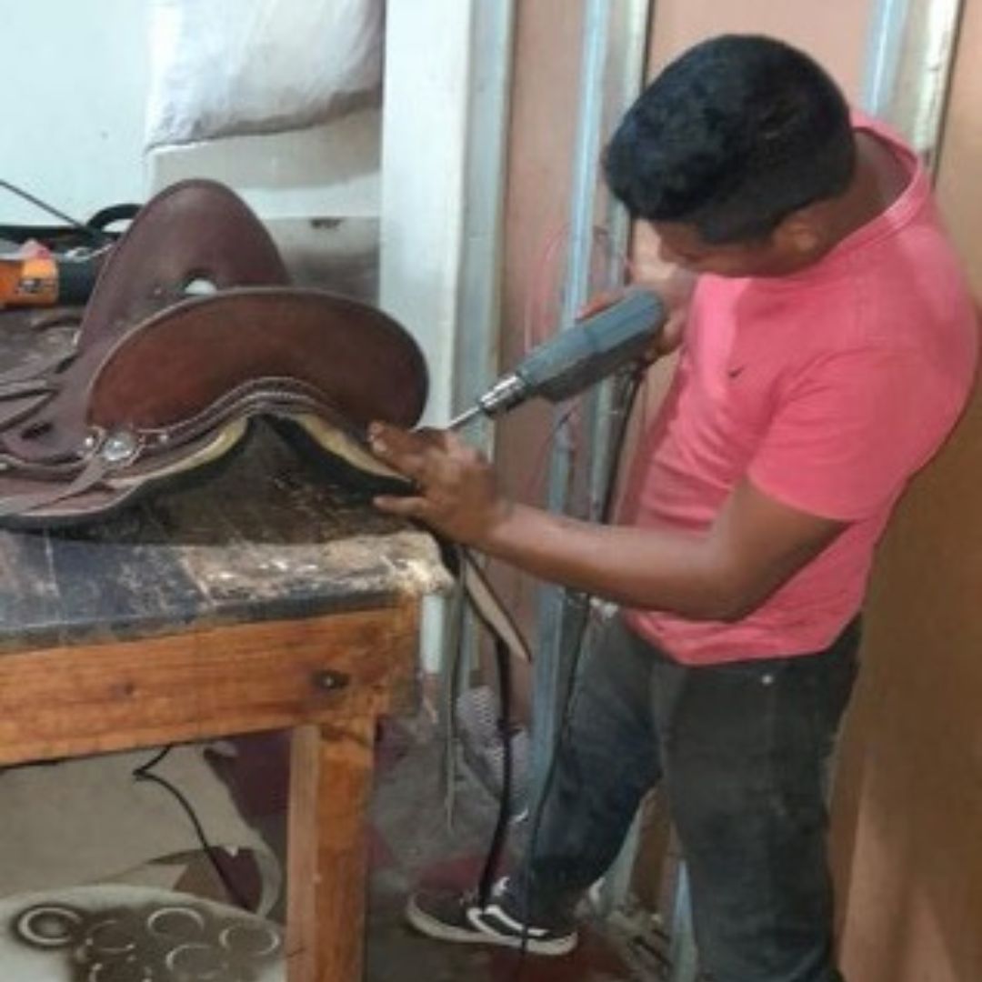 a man works on a leather saddle