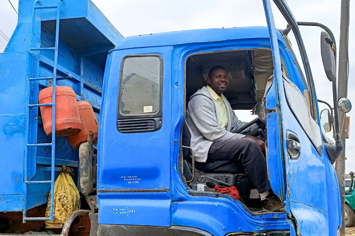 a man smiles from his seat in the cab of a dump truck