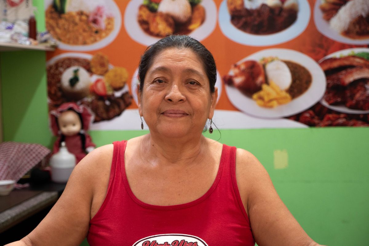 a woman in a red shirt in front of a wall with pictures of different foods