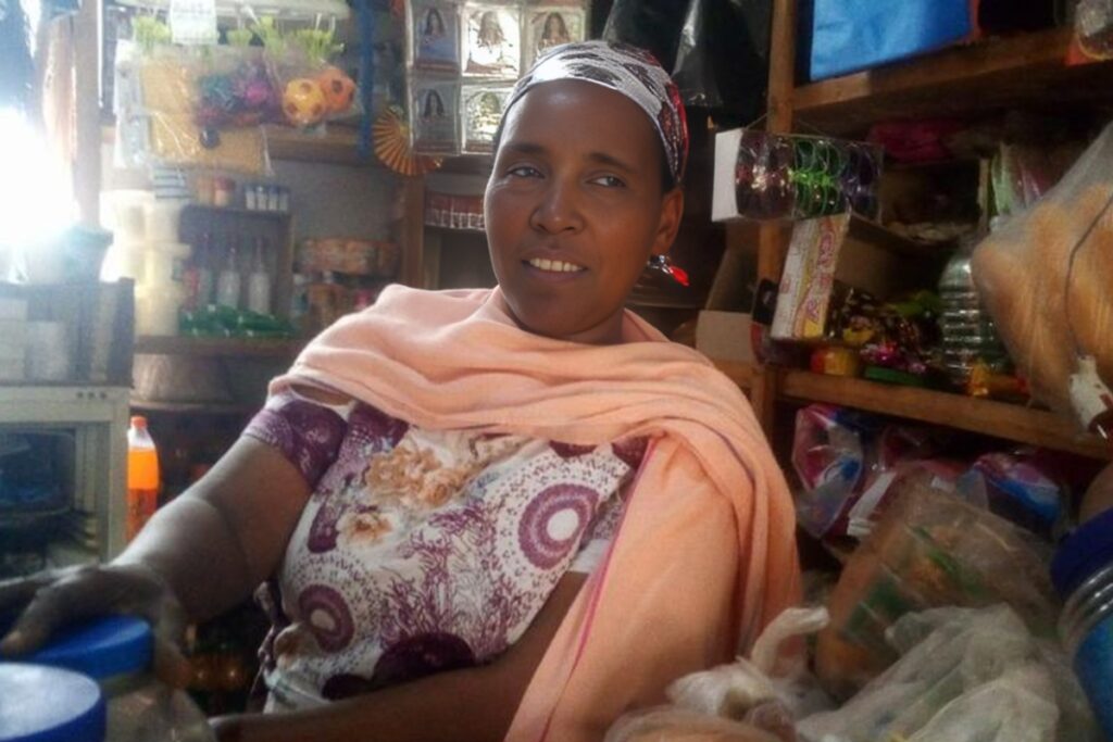 a woman smiles in front of shelves of convenience store merchandise
