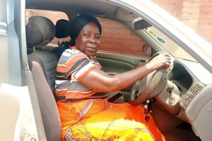 a woman in an orange skirt and shirt sits in the driver's seat of a car