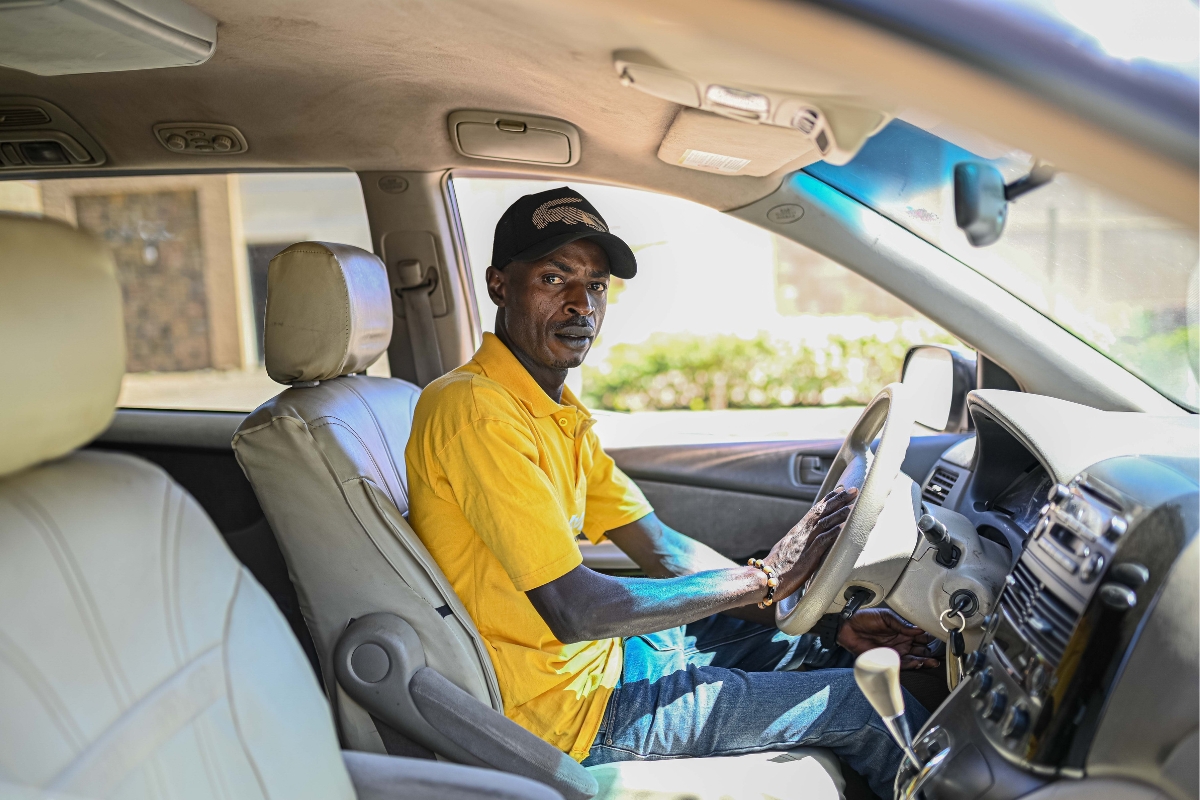 a man in a yellow shirt sits in the driver's seat of a car
