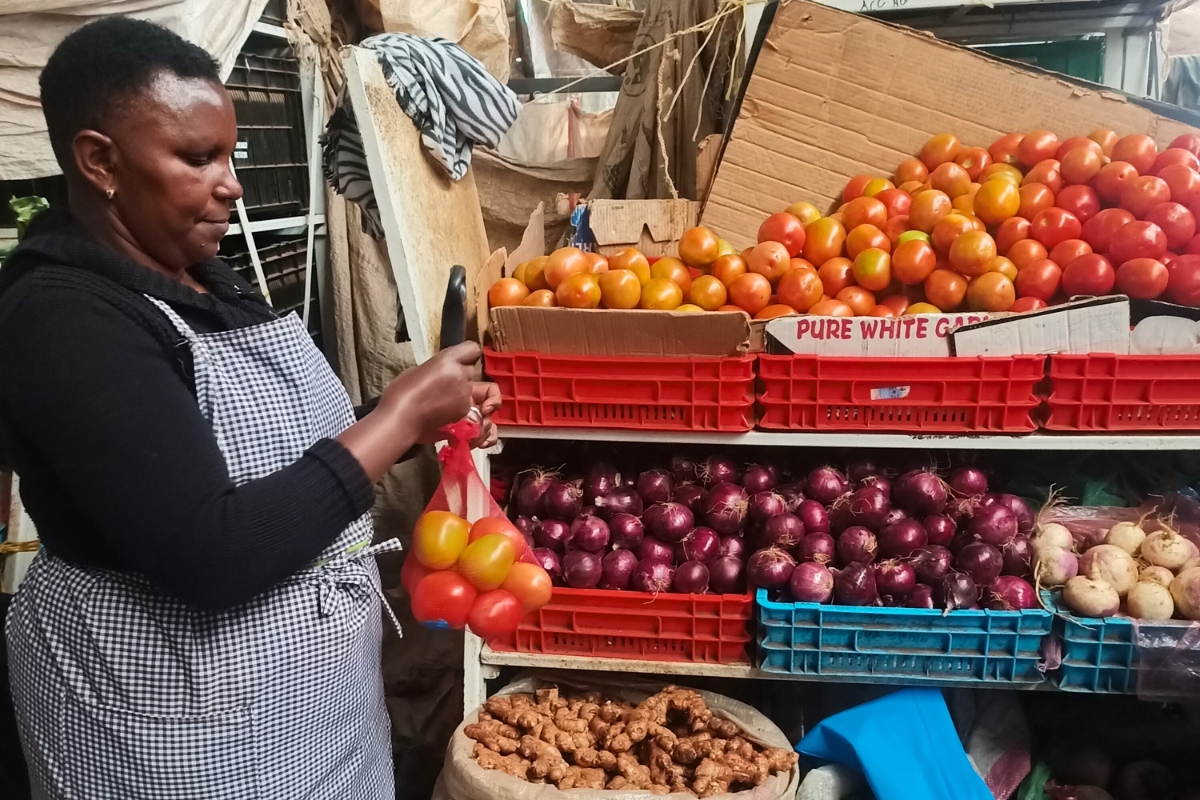a woman ties a bag of tomatoes in front of a market stall of produce
