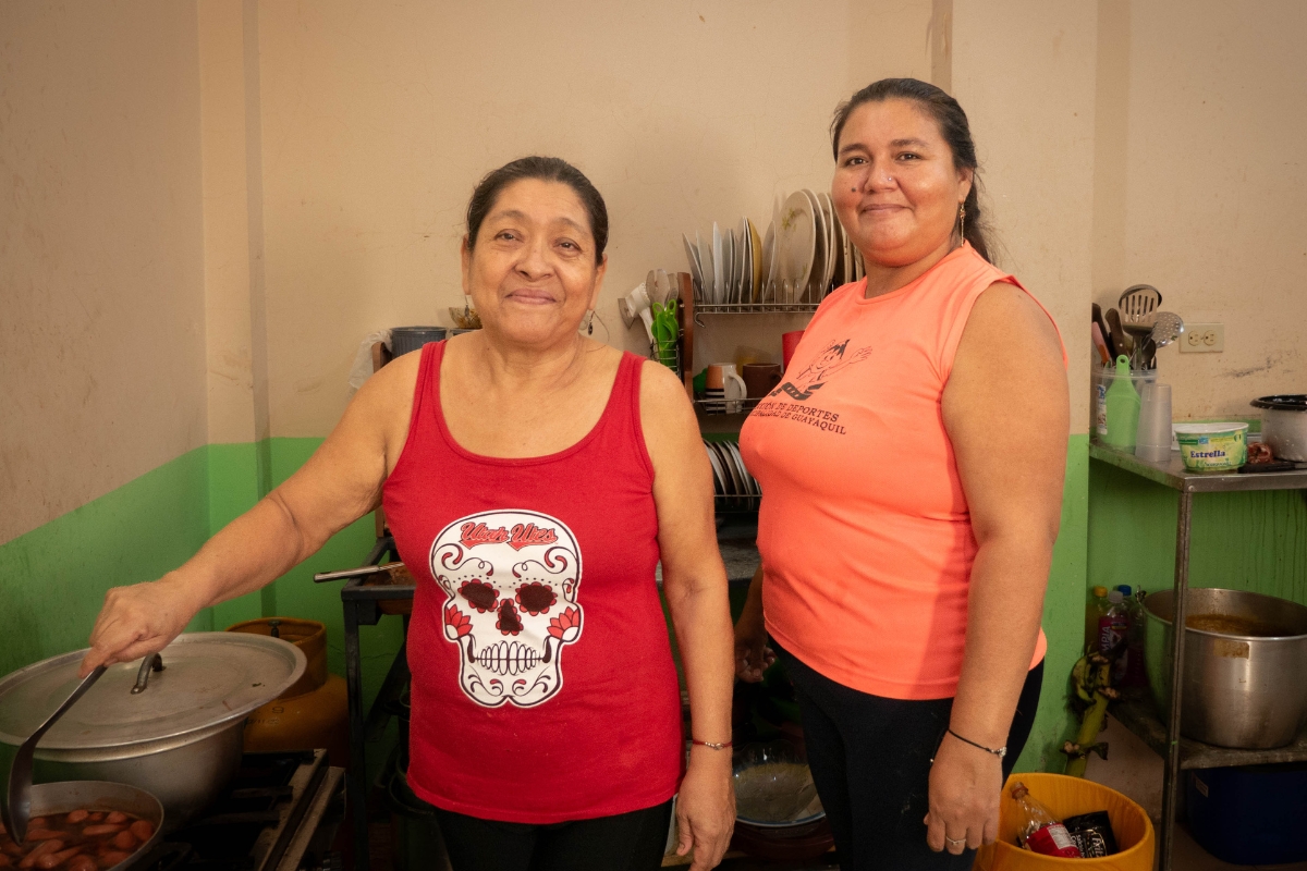 two women stand in a kitchen next to a pot on the stove