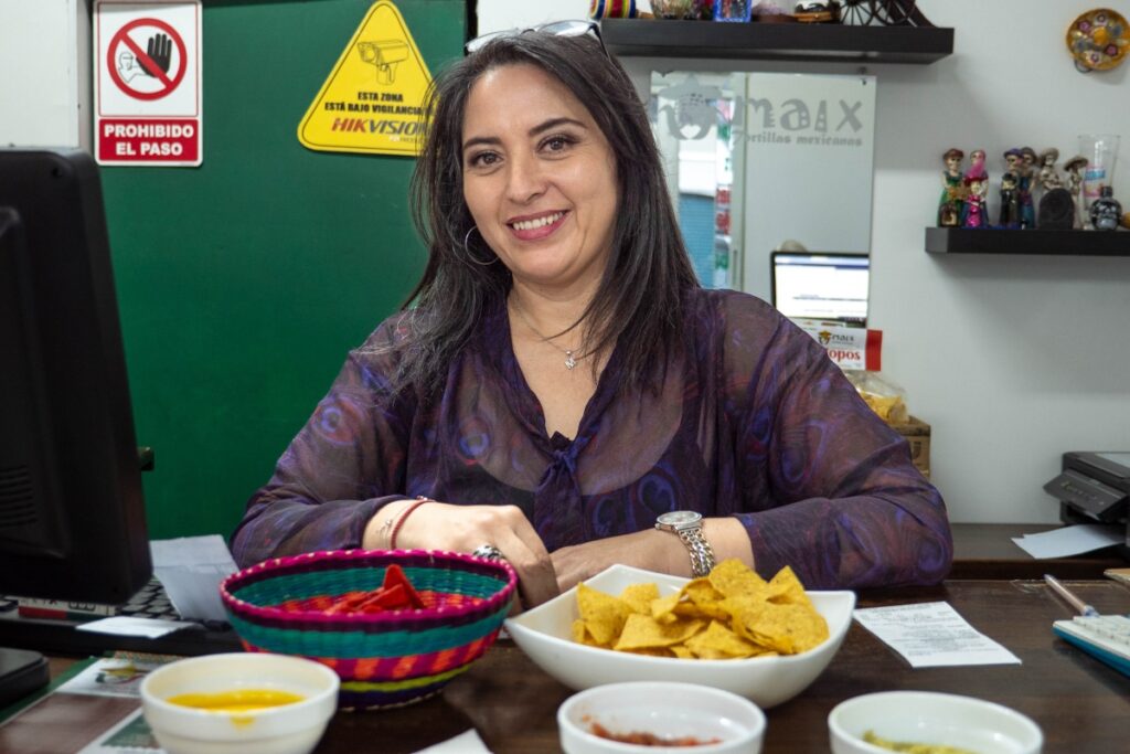 a woman smiles at counter top with bowls of chips and salsa