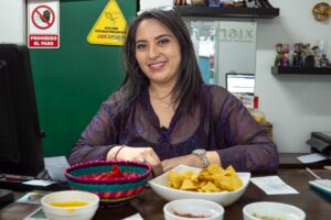 a woman smiles at counter top with bowls of chips and salsa