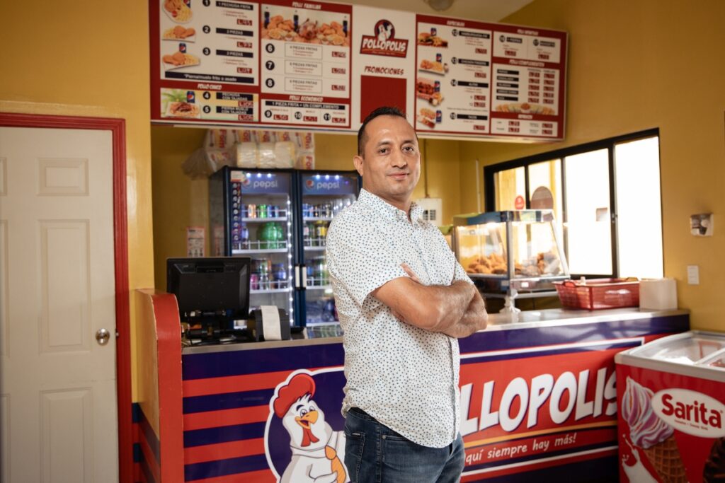 a man stands with arms crossed and smiling in front of a restaurant counter