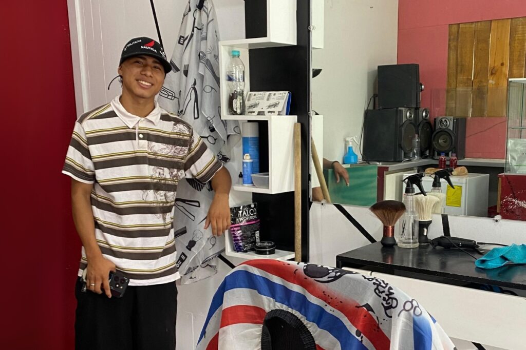 a young man stands next to a barber chair and mirror