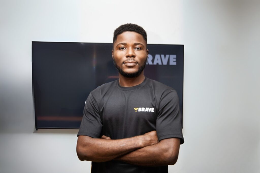 a man stands with arms crossed in front of a tv display on a white wall