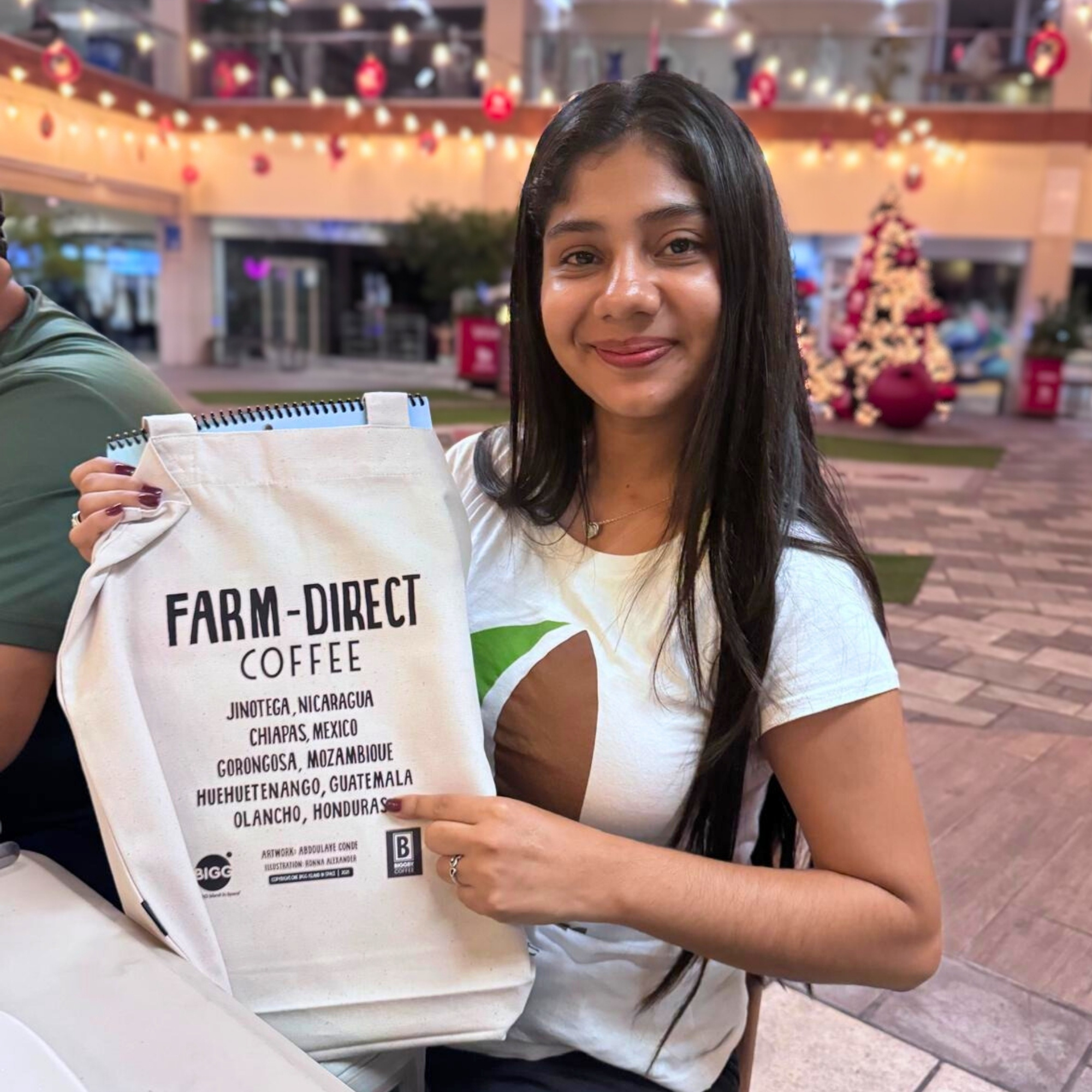 a young woman points at a bag that says "Farm Direct Coffee" and lists "Olancho, Honduras" underneath