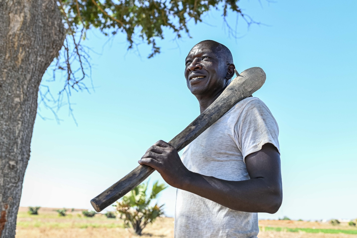 a man stands looking up into the distance with a farm tool on his shoulder