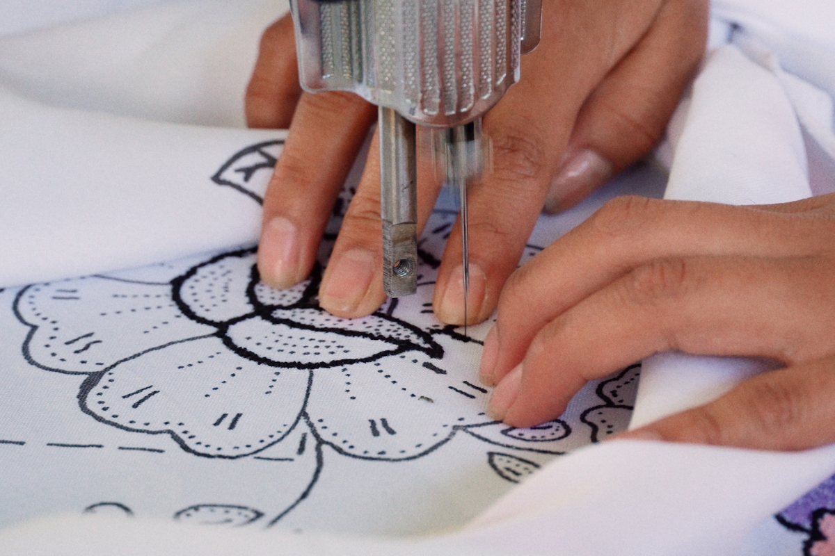 hands guiding fabric with an embroidered flower under a sewing machine needle