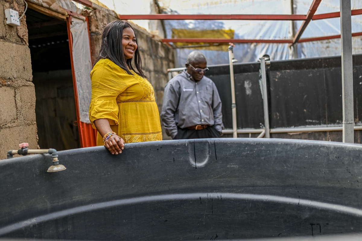 a woman stands with a hand resting on a large black plastic tank