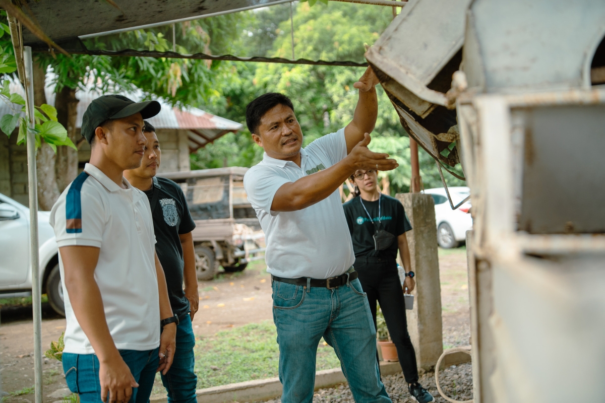 a man points to piece of metal equipment while two men and a women look on