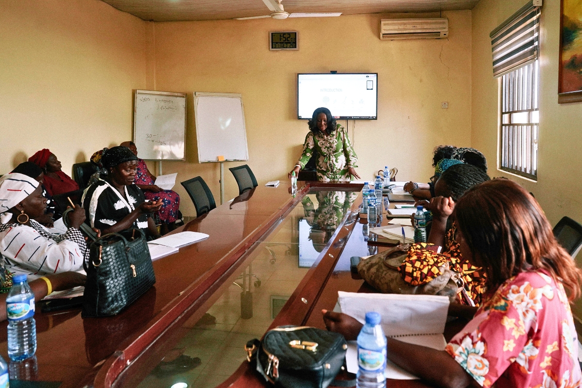 a woman stands at the end of a table presenting to other women gathered around the table