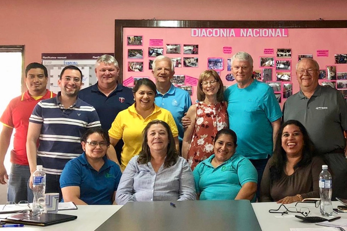 Group of people smile together in front of a bulletin board.