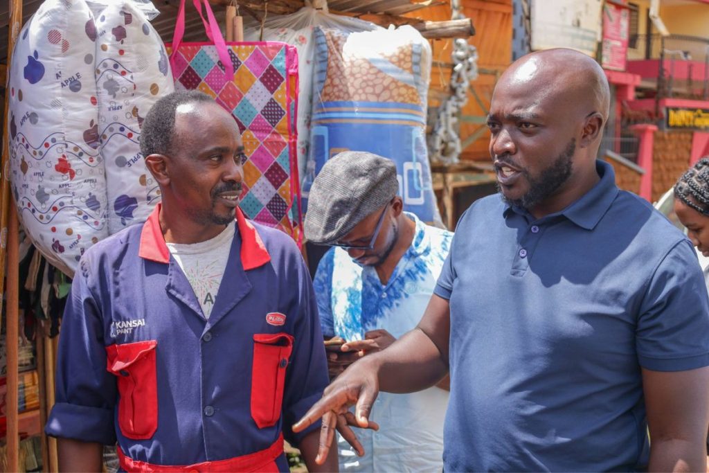 Two men stand talking together in a marketplace