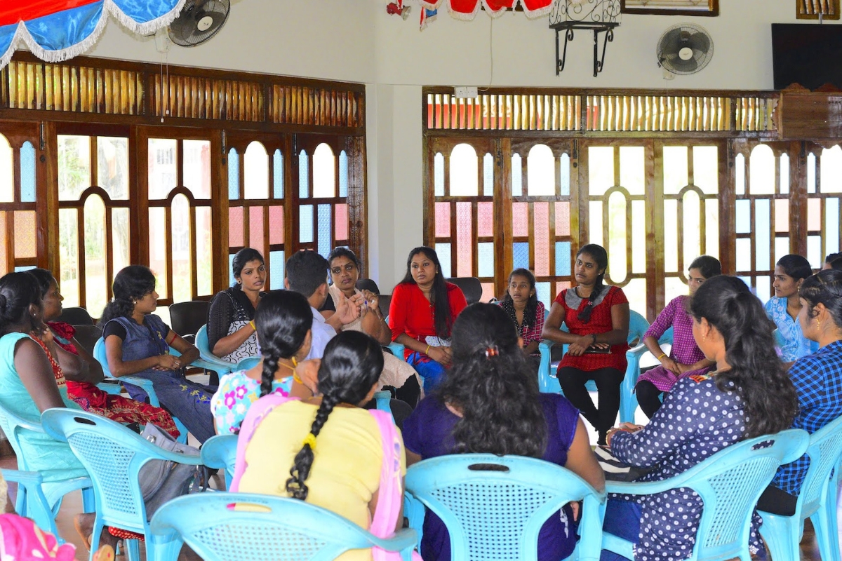 Group of women sit in blue chairs together in a circle talking.