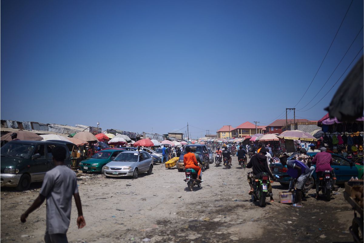 marketplace with people riding mopeds, cars, and umbrella stands